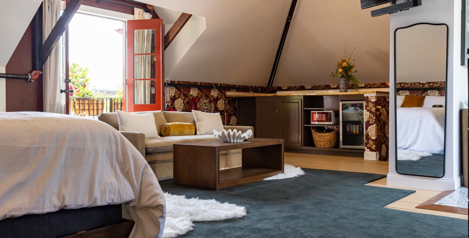 Cozy attic room featuring a bed, seating area, and large windows with red shutters.