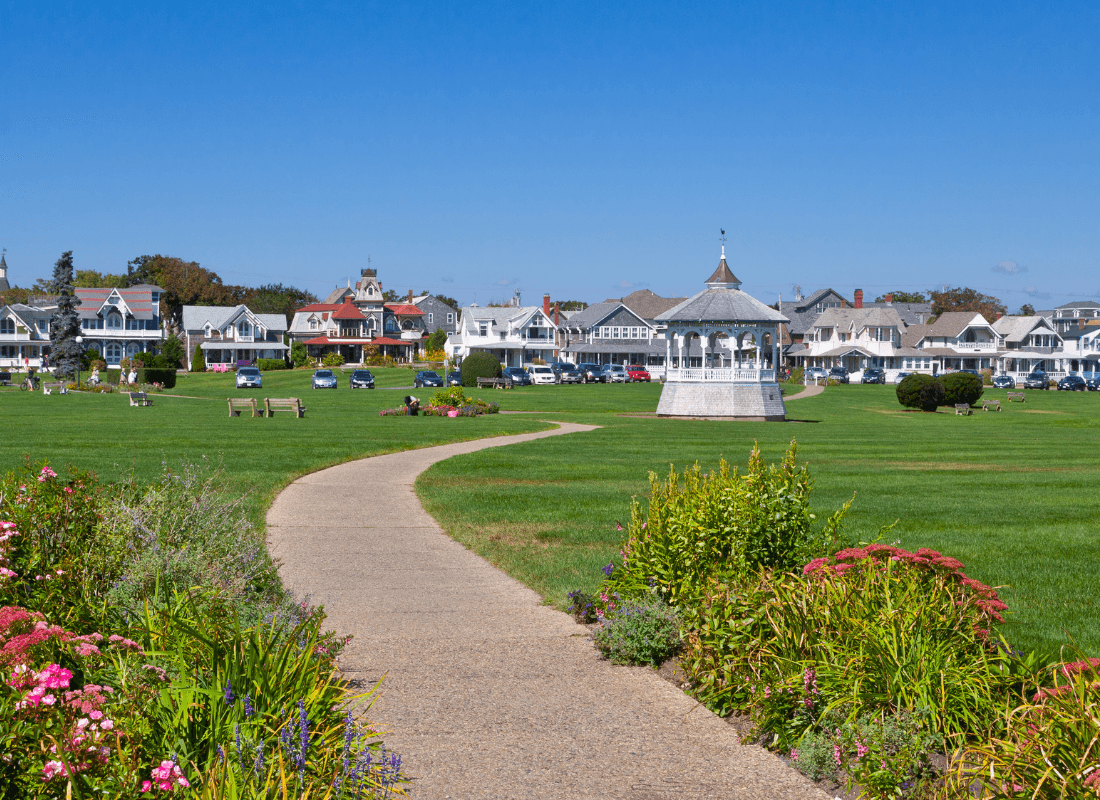 A landscaped park features a winding path leading to a gazebo, surrounded by colorful flowers and historic homes.